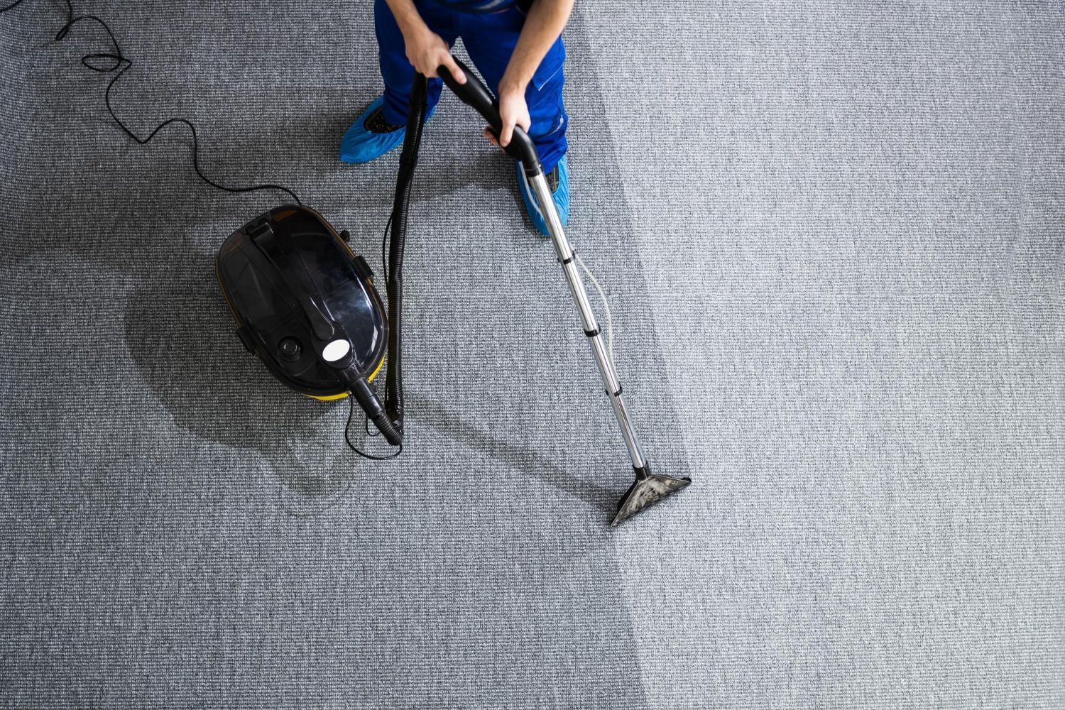A person is cleaning a carpet with a vacuum cleaner.