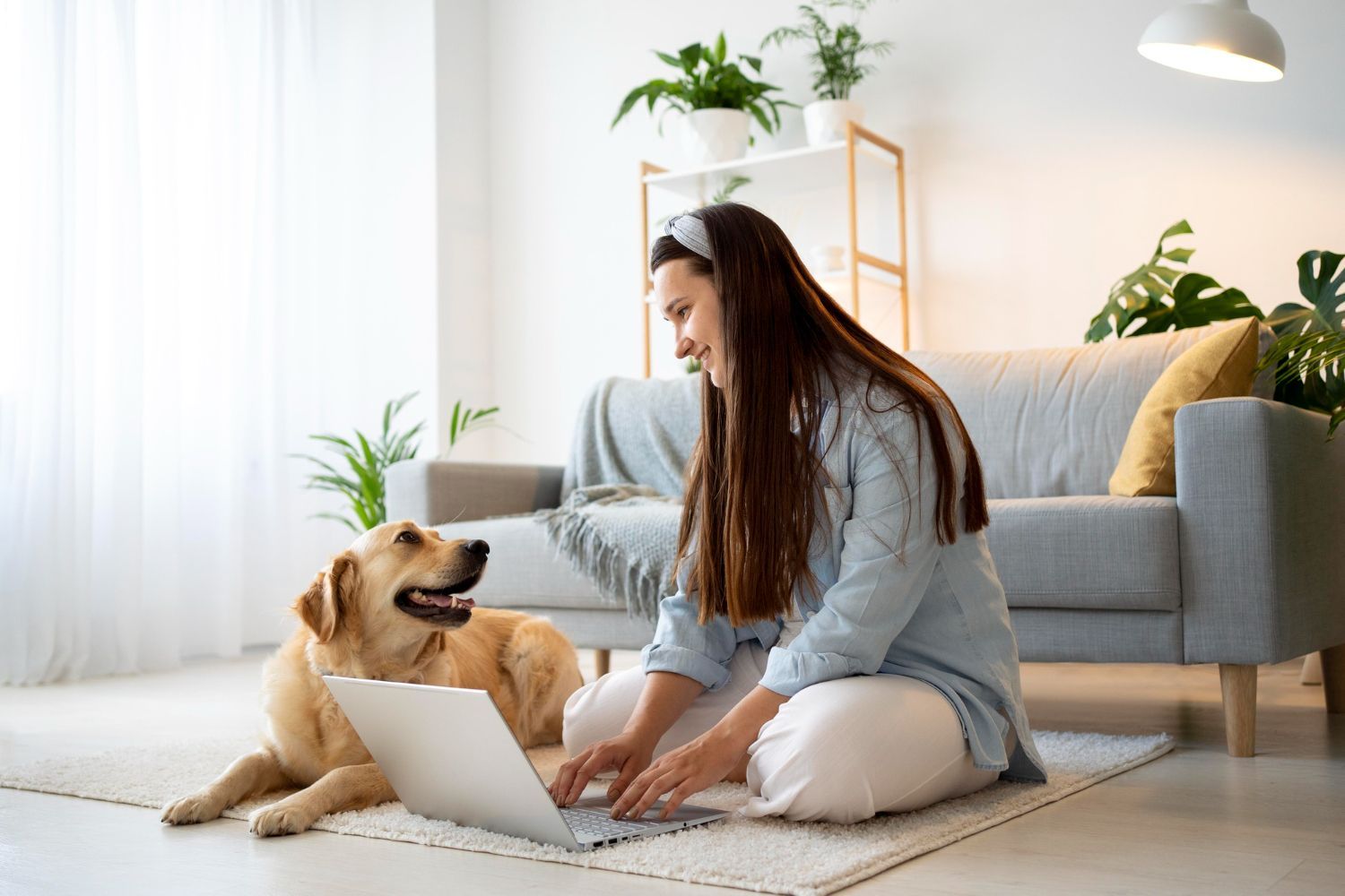 A woman is sitting on the floor with her dog and using a laptop.